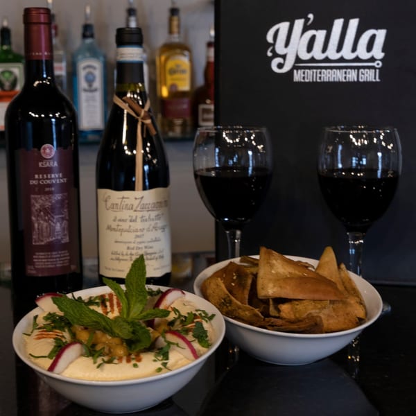 Yalla Grill's hummus with radishes and mint, pita chips, red wine, and bottles of wine.