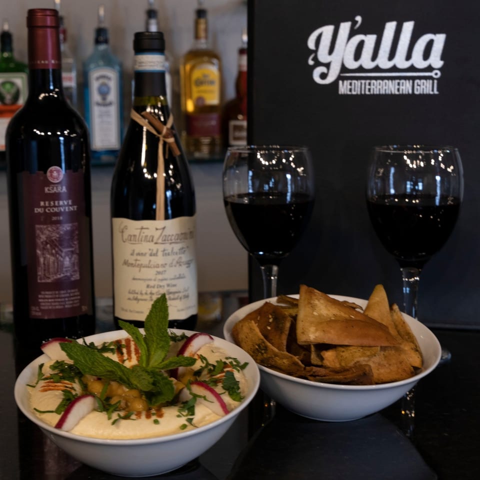 Yalla Grill's hummus with radishes and mint, pita chips, red wine, and bottles of wine.