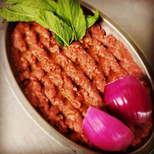 Lebanese raw kibbeh with fresh mint leaves and pickled red onions in an oval dish.