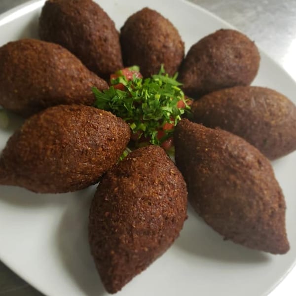 Eight fried kibbeh, football-shaped, arranged around a small salad of chopped tomatoes and parsley.