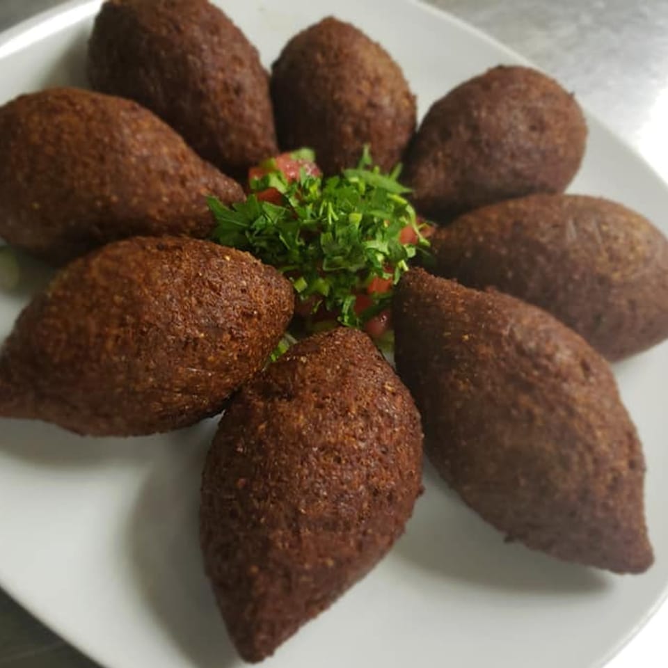 Eight fried kibbeh, football-shaped, arranged around a small salad of chopped tomatoes and parsley.