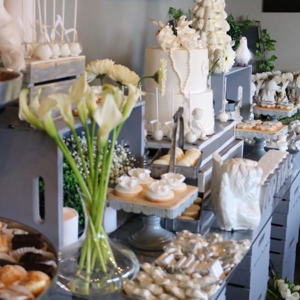 A dessert table with a white tiered cake, cookies, cake pops, and calla lilies.