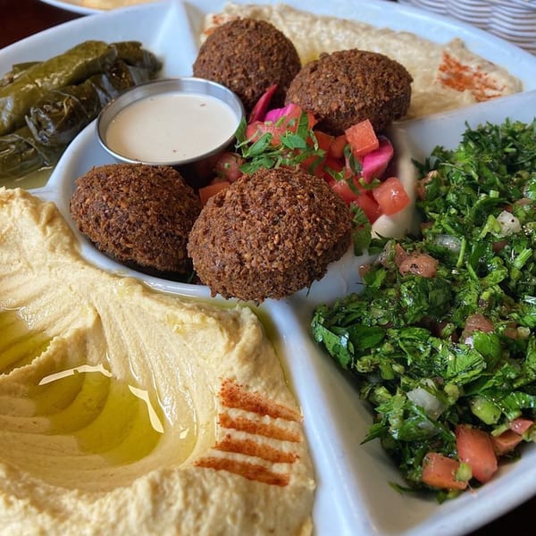 A Yalla Grill Lebanese platter with falafel, hummus, tabbouleh, stuffed grape leaves, and dipping sauce.