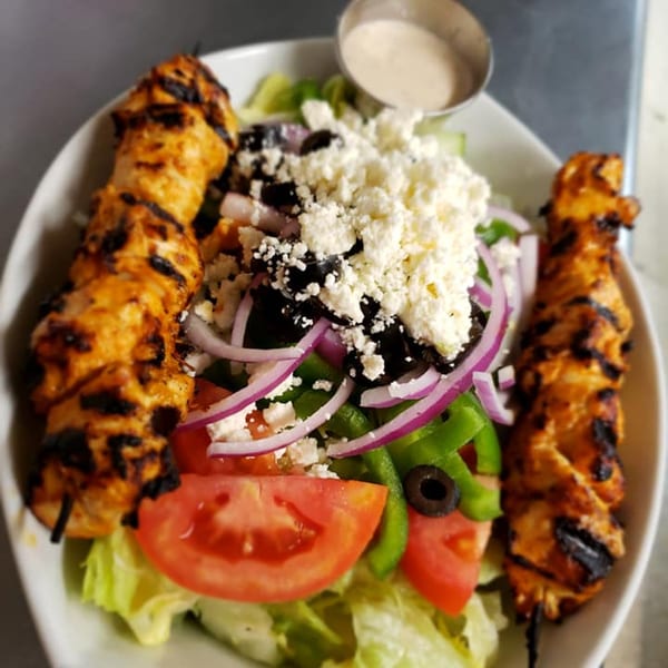 Two chicken shish tawook skewers flank a vibrant Lebanese salad with feta, olives, and red onion.