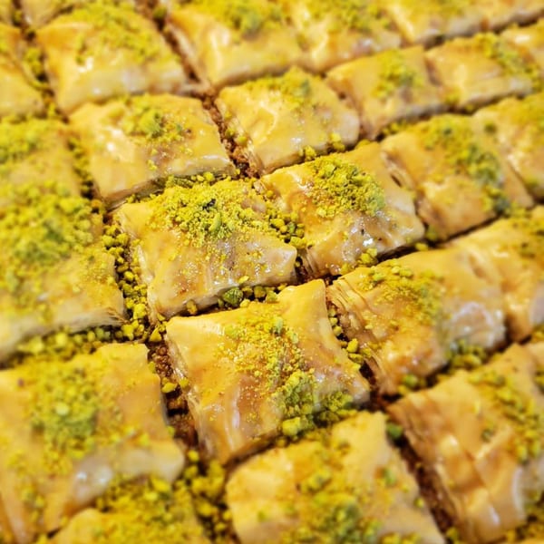 Close-up of golden Lebanese baklava pastries, drizzled with syrup and sprinkled with green pistachios.