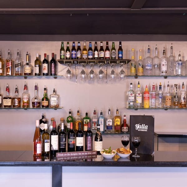 A well-stocked bar at Yalla Grill, featuring various liquor bottles, beers, and wine on shelves.